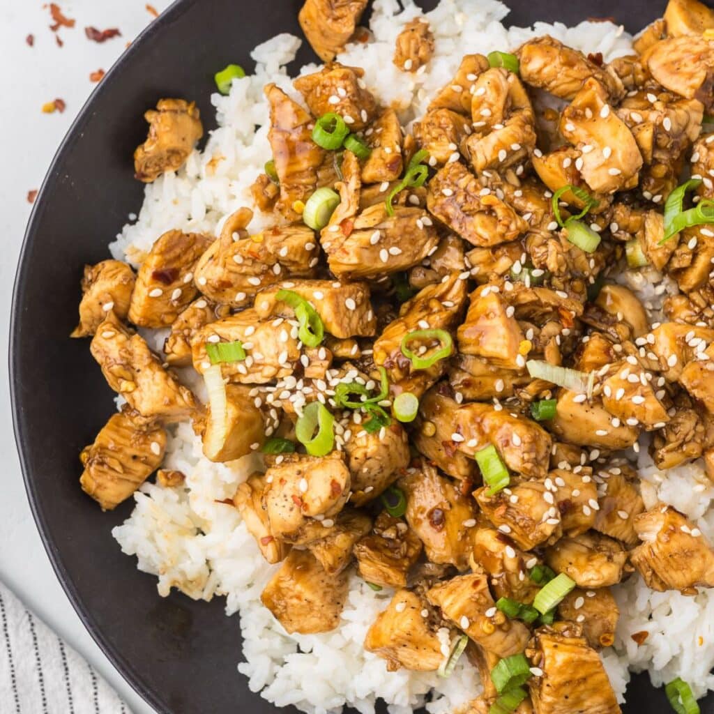 Spicy Teriyaki Chicken served over a bed of rice in a black bowl.