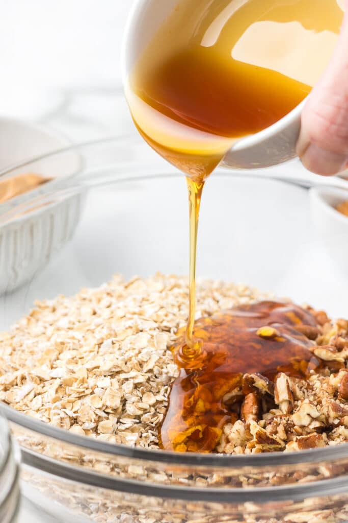 Honey being poured into a bowl with oats and pecans.
