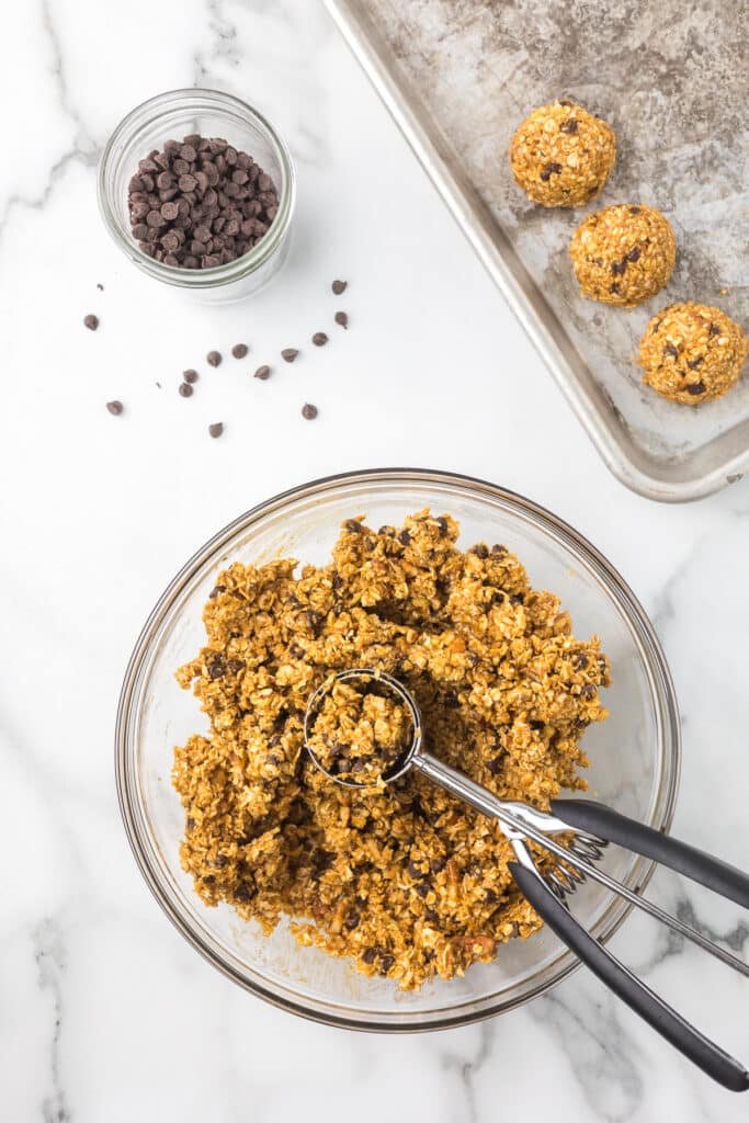 Ingredients to make pumpkin protein balls in a bowl with a cookie scoop.