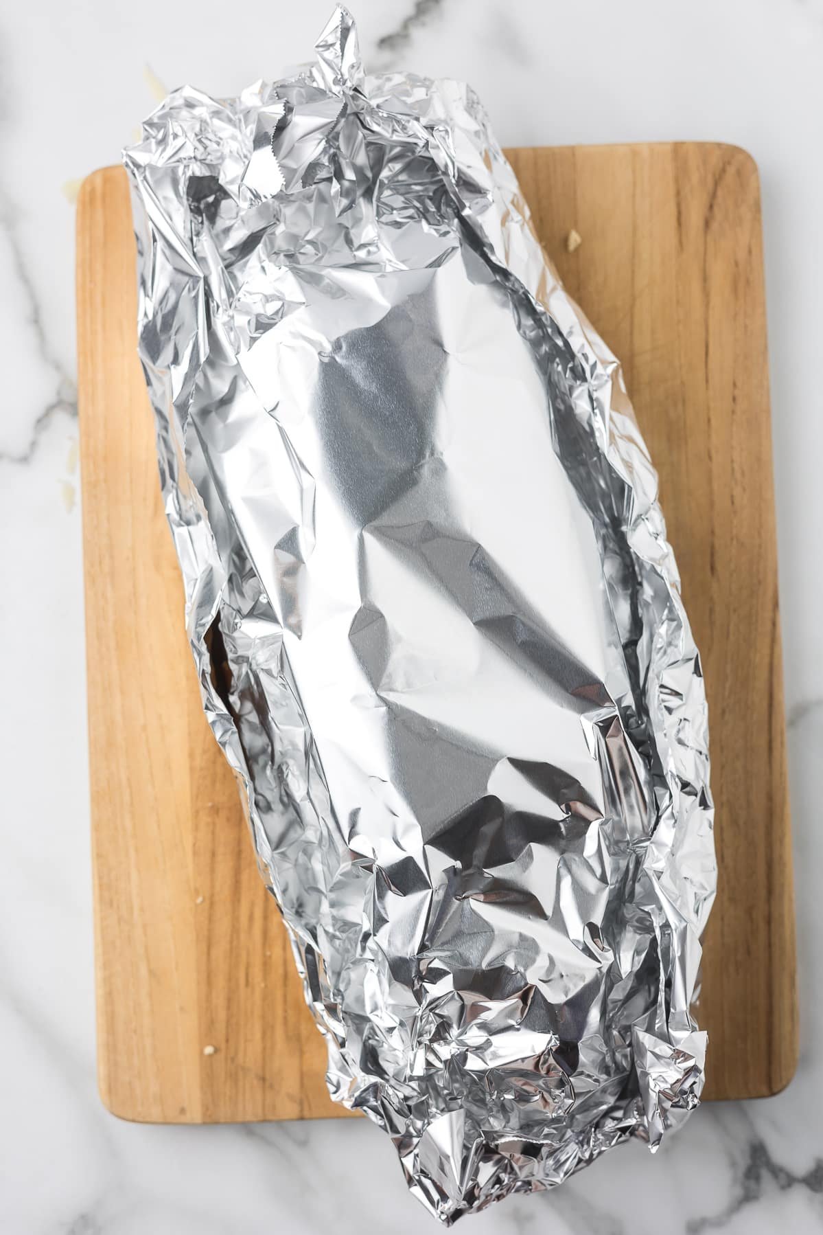 Stuffed garlic bread wrapped in foil and placed on a baking sheet before going into the oven.