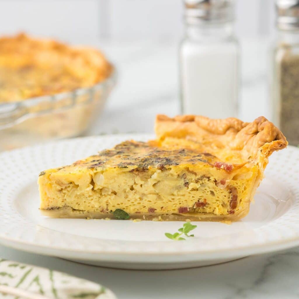 Onion and bacon quiche on a white plate with salt and pepper shakers.