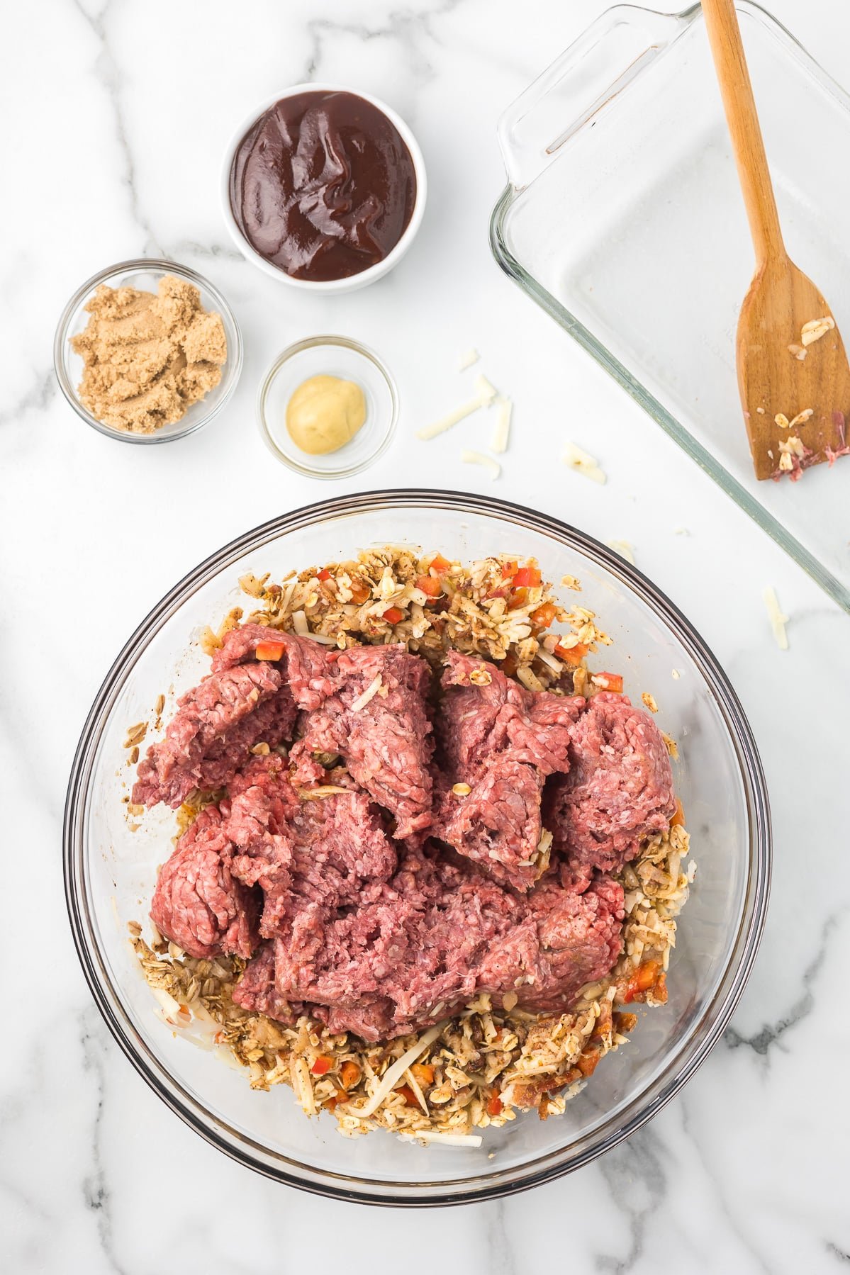 Ground beef being added to the oat mixture in a clear mixing bowl.