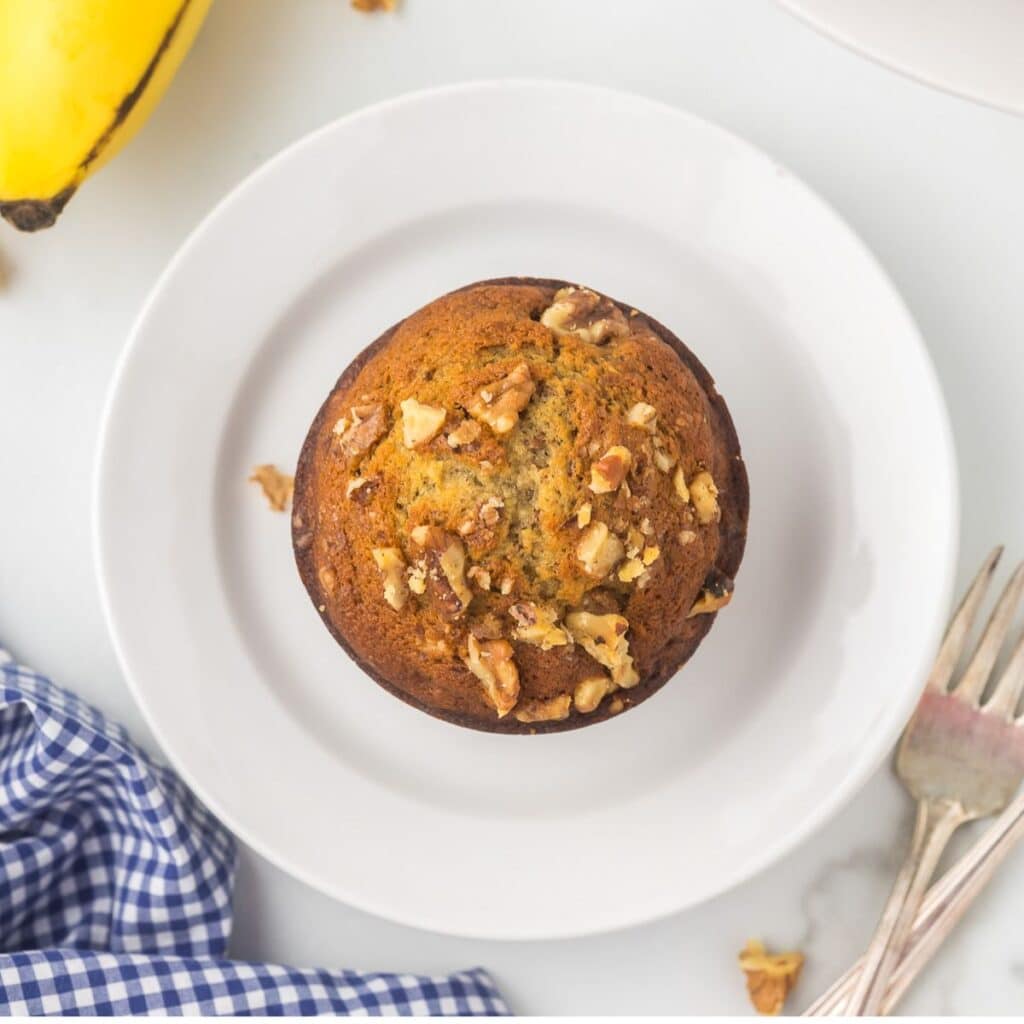 Jumbo Banana Muffin on a white plate with bananas peaking in the picture.