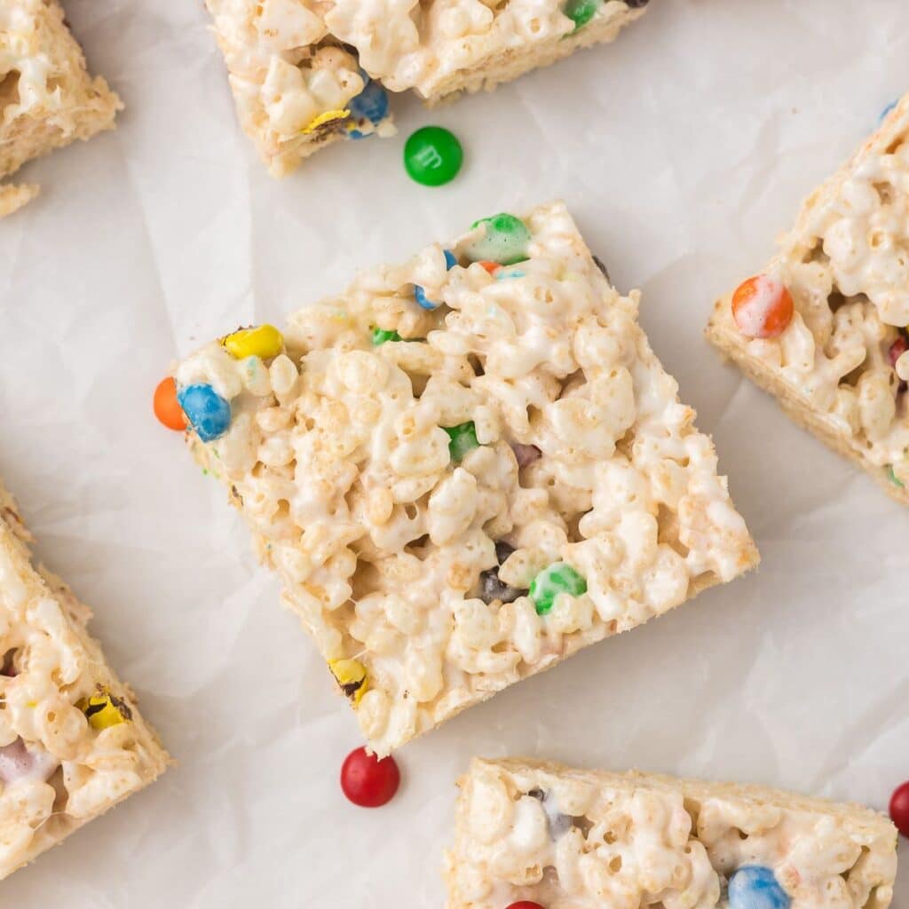 Mini M&M Rice Krispie treats cut into squares on parchment paper.