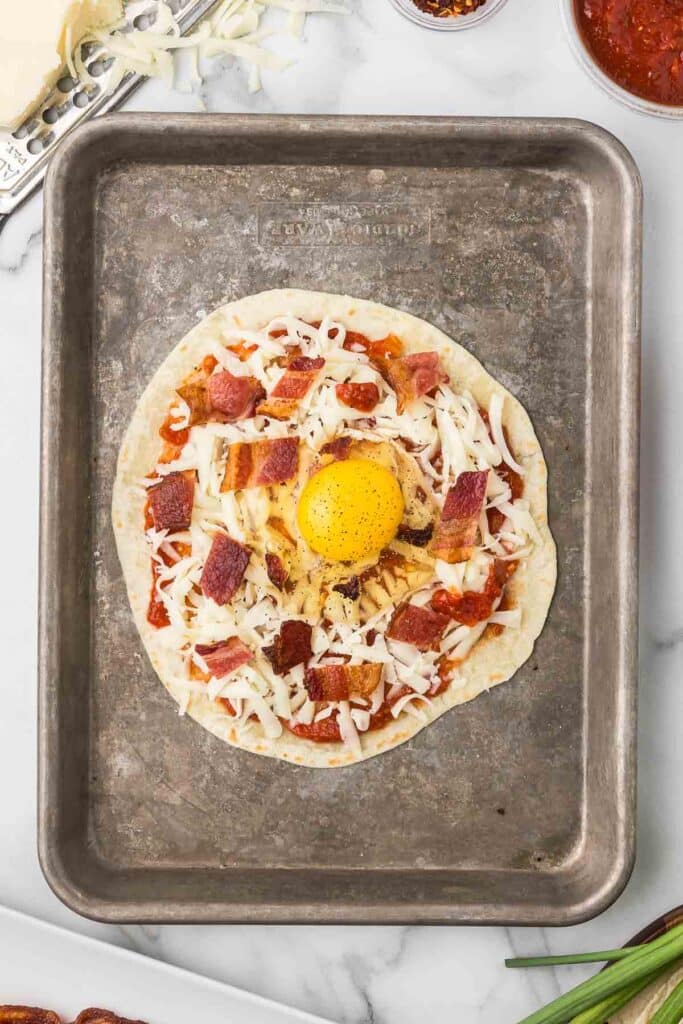 A tortilla with pizza sauce, bacon, cheese and a raw egg.