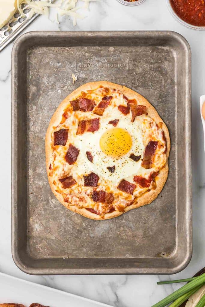 A tortilla with pizza sauce, bacon, cheese and an egg after it has come out of the oven.