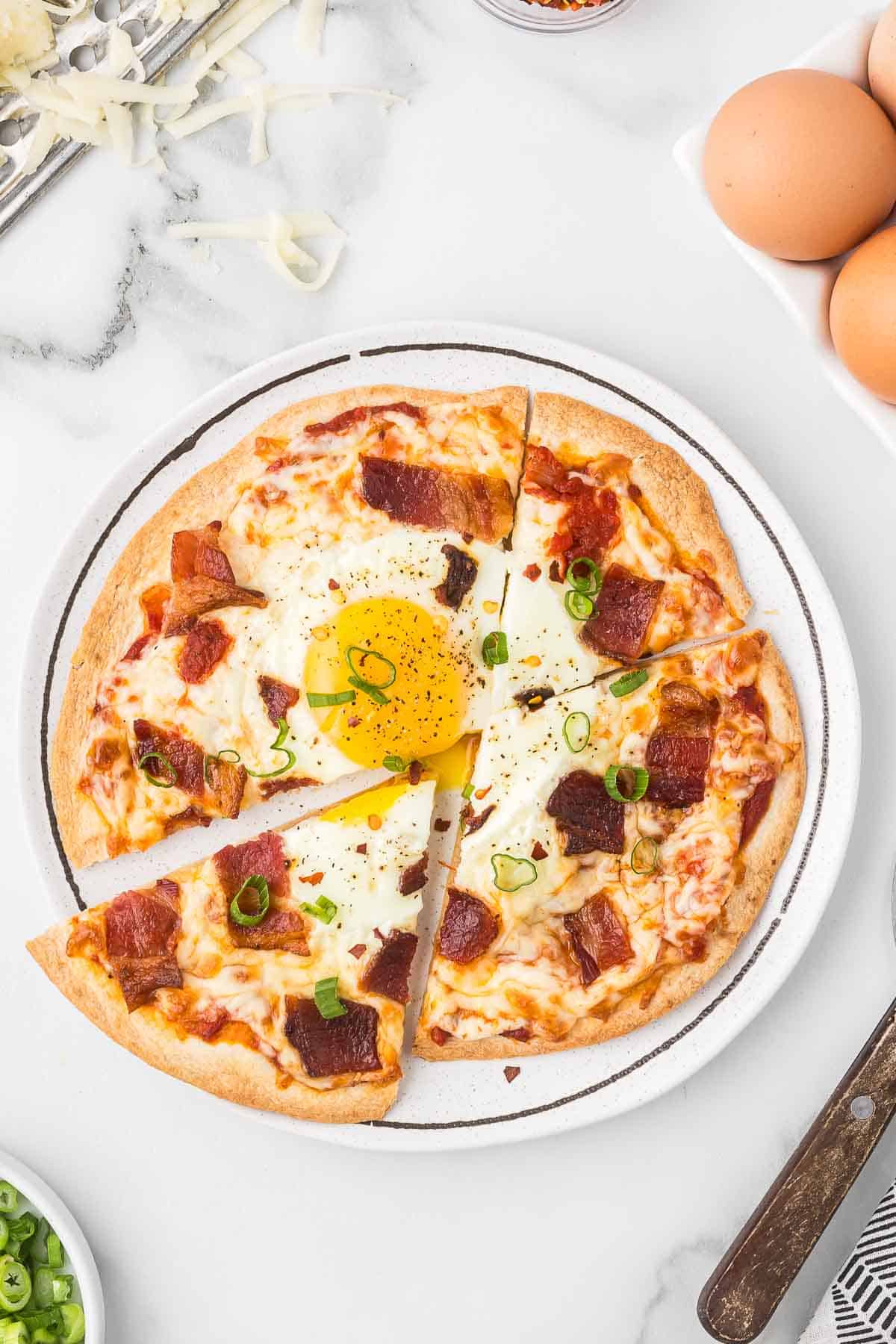 Breakfast Pizza on a white plate with eggs and bacon.