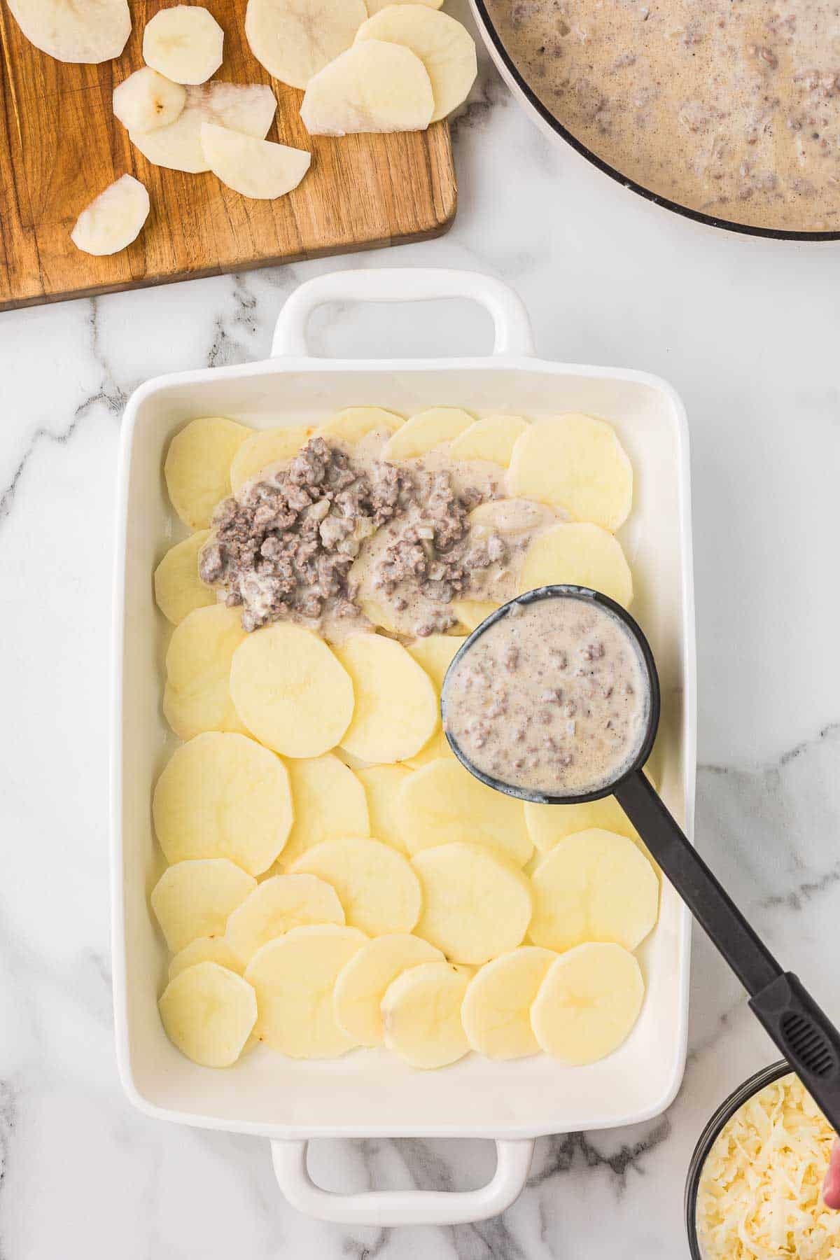 Sliced potatoes lined on the bottom of a casserole dish with ground beef cream sauce being added in layers.