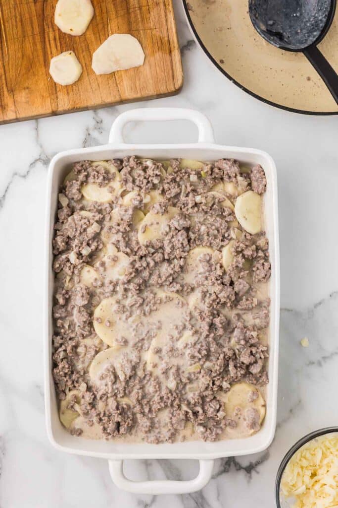 A casserole dish with potatoes and ground beef sauce mixture before baking.