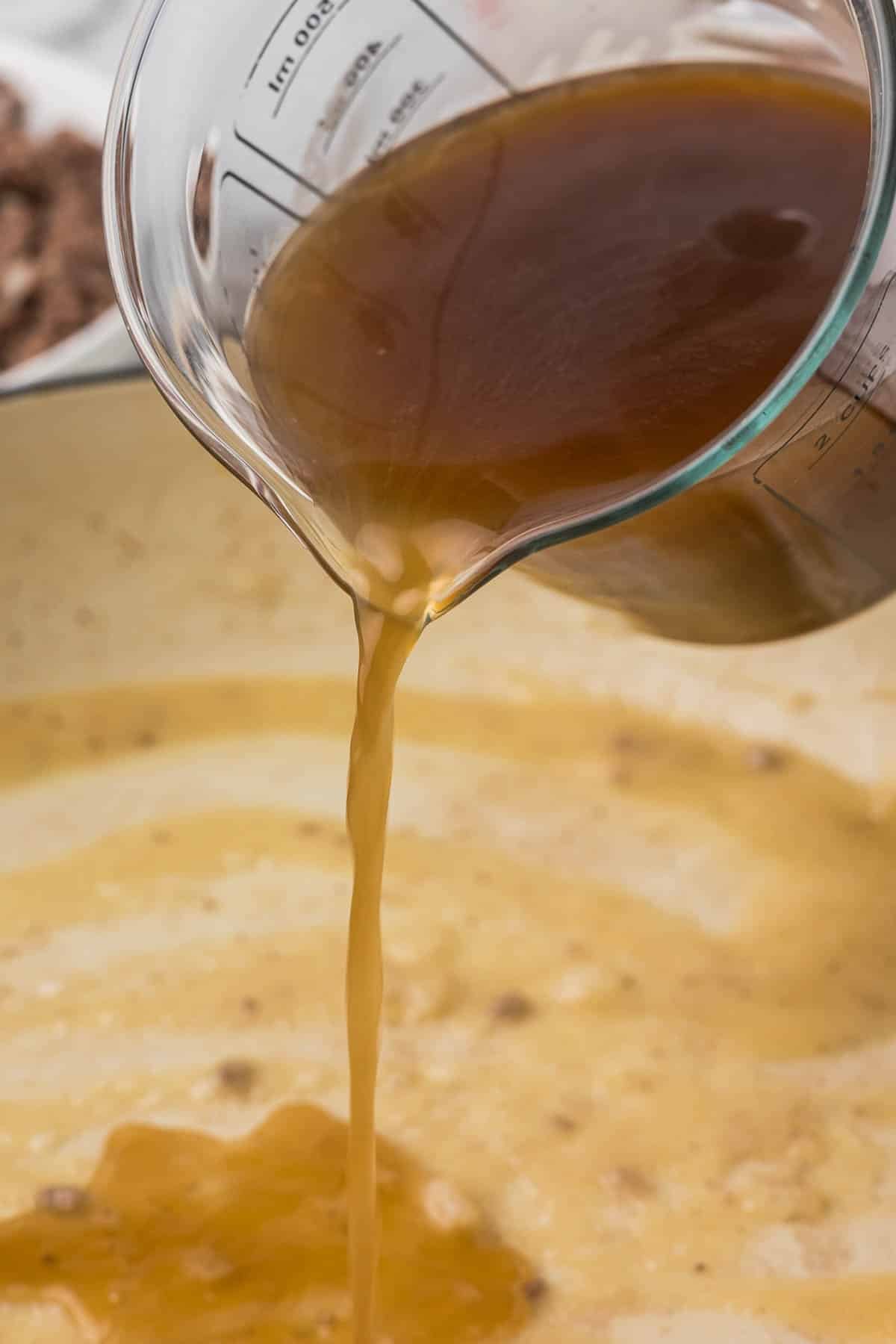 Beef broth being poured into a pan with a butter and flour mixture.