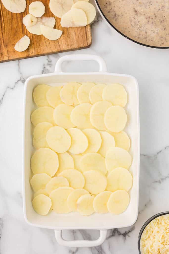 Sliced potatoes lined on the bottom of a casserole dish.