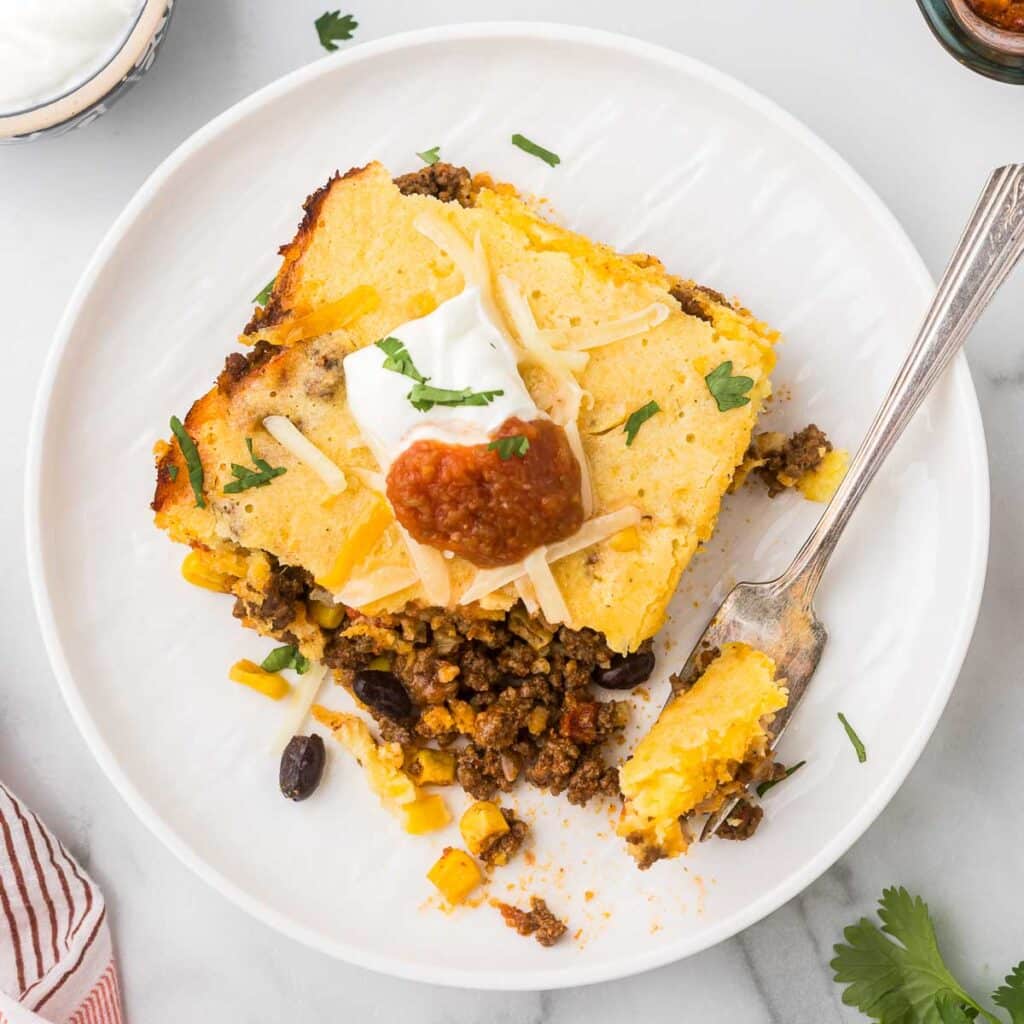 Cowboy Cornbread Casserole on a plate with sour cream and salsa.