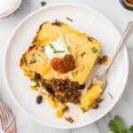 Cowboy Cornbread Casserole on a plate with sour cream and salsa.