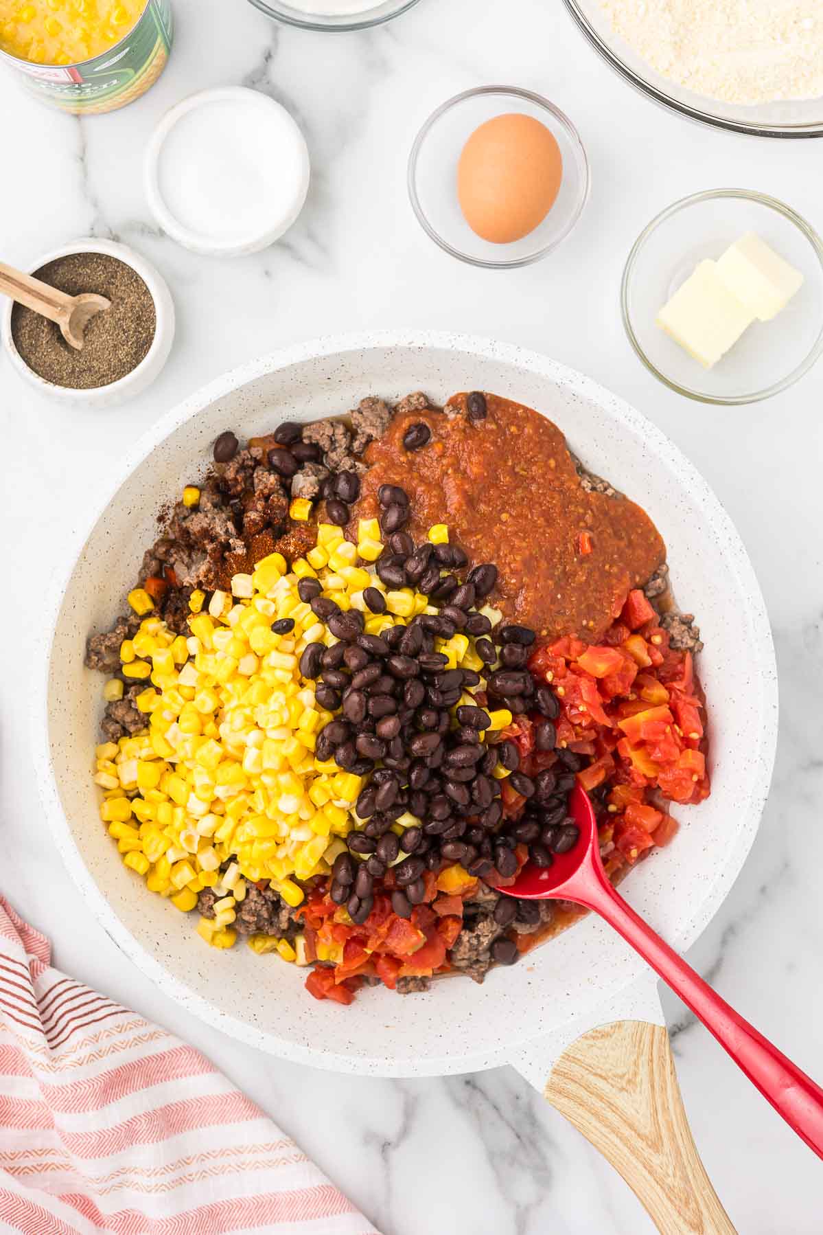 Ingredients in a skillet to make cowboy casserole including salsa, corn, tomatoes, black beans, ground beef and salsa.