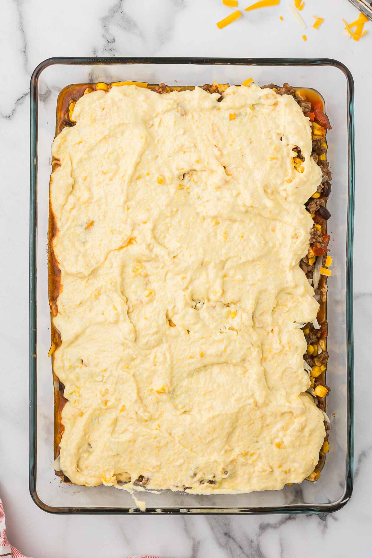 Ingredients for cowboy cornbread casserole layered in a glass casserole dish before baking.