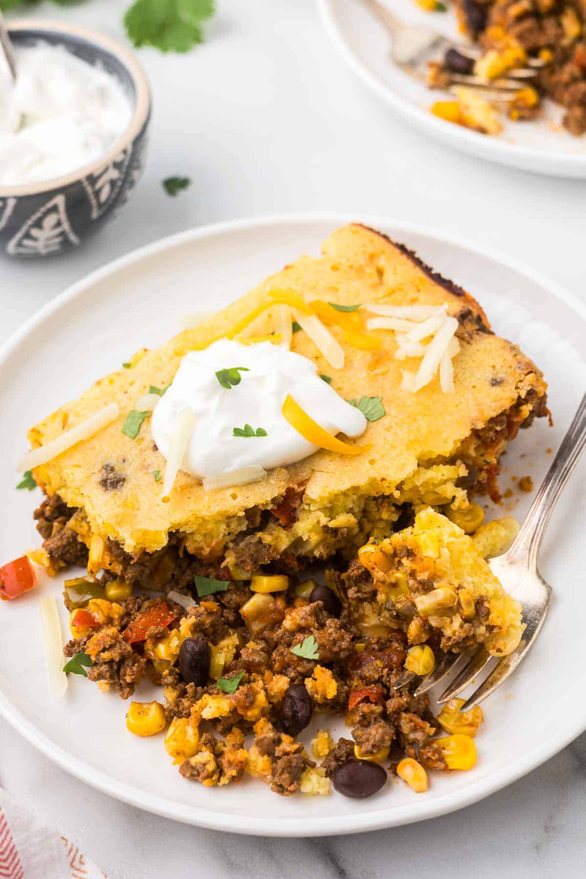 Cowboy Cornbread Casserole on a plate with cheese and sour cream.