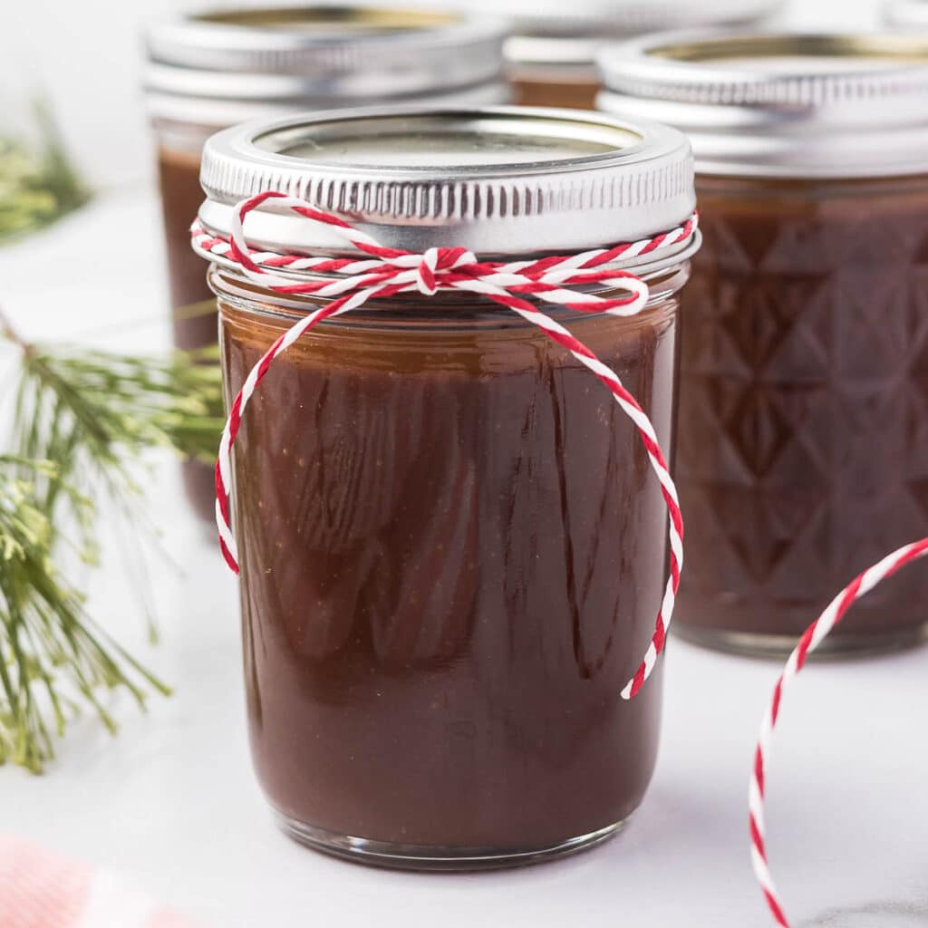 Hot fudge sauce in a mason jar with a red and white ribbon for gift giving.