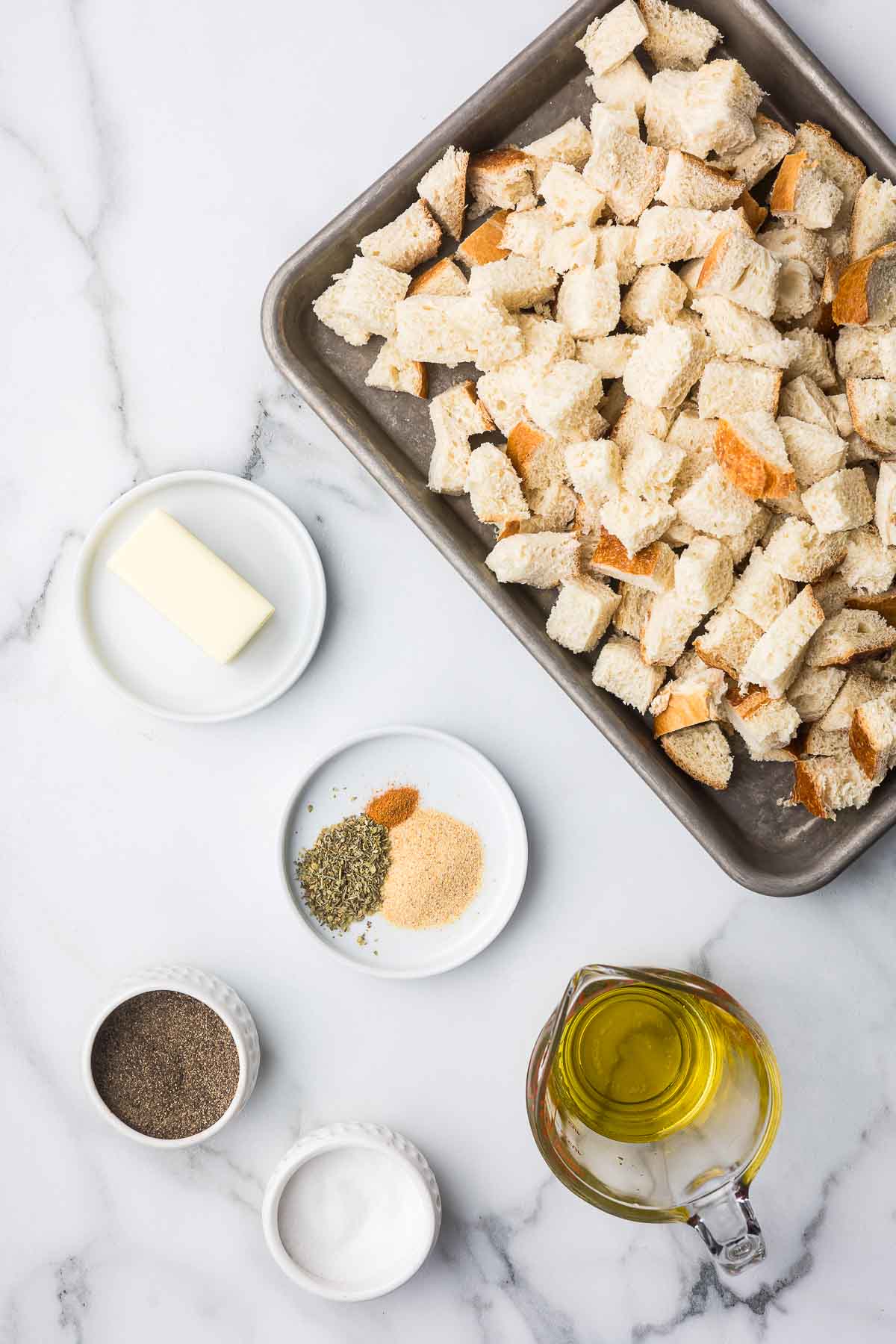 Ingredients to make air fryer croutons including cubed bread, olive oil, butter and spices.