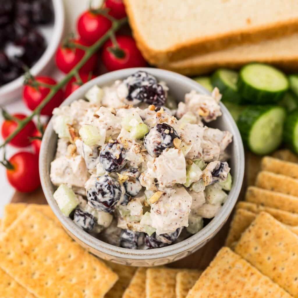 Cranberry nut chicken salad in a bowl with crackers,m bread and vegetables.