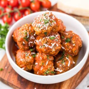 Baked Italian Meatballs in a white bowl with tomatoes in the background.