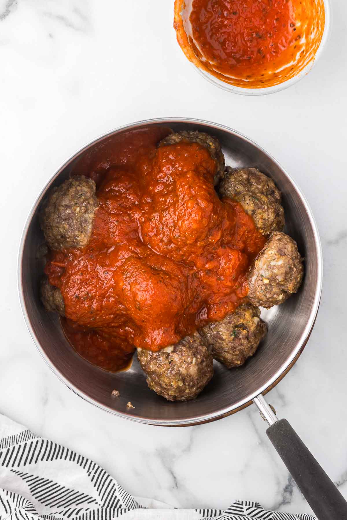 Baked meatballs in a sauce pan with marinara sauce.