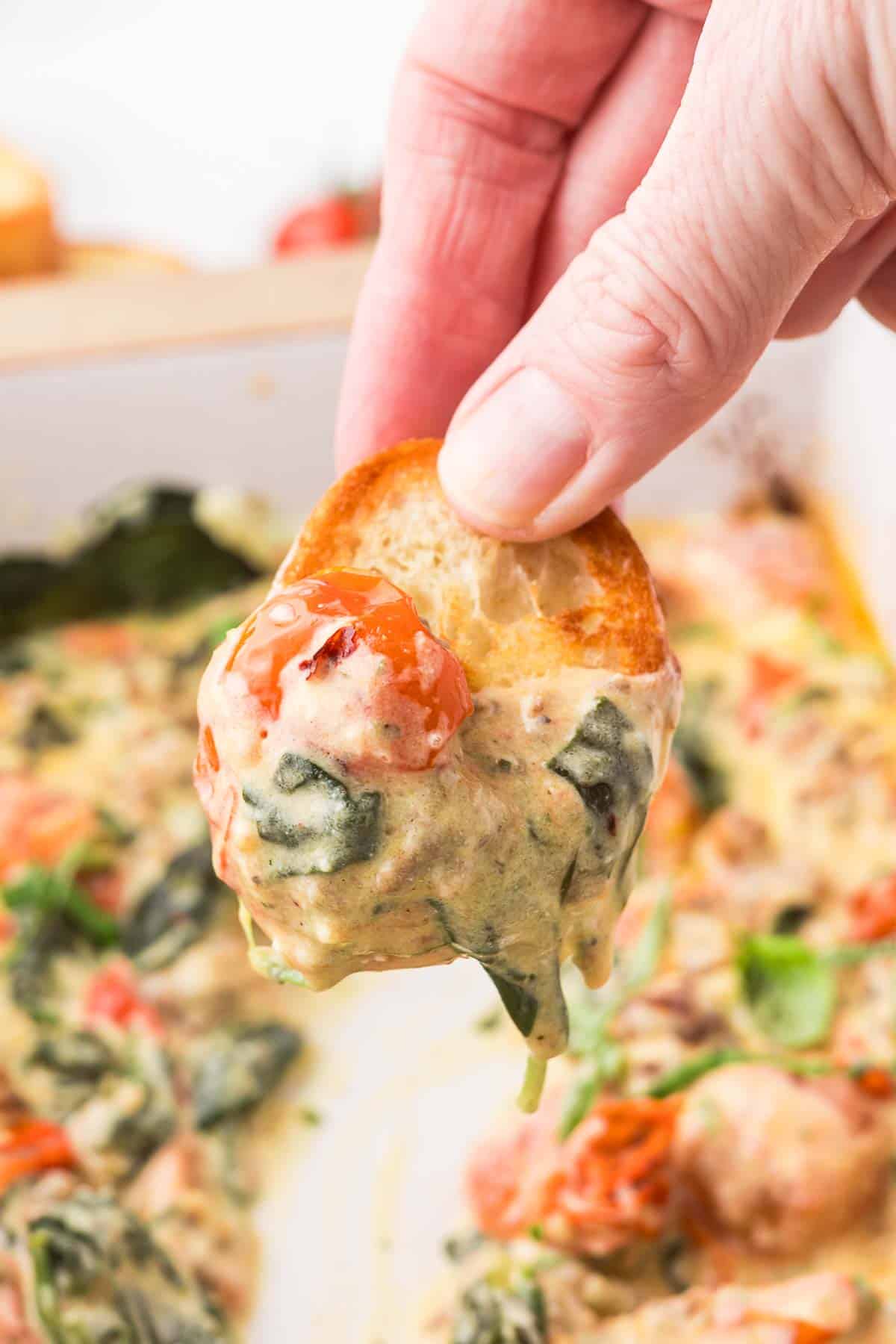 Baguette slice dipped in Boursin cheese dip with spinach, fresh basil and cherry tomatoes.