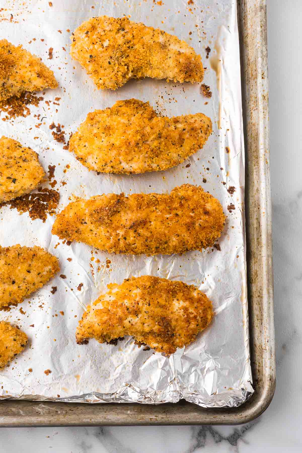 Chicken tenders coated in parmesan cheese and panko breadcrumbs after they have cooked on a sheet pan.
