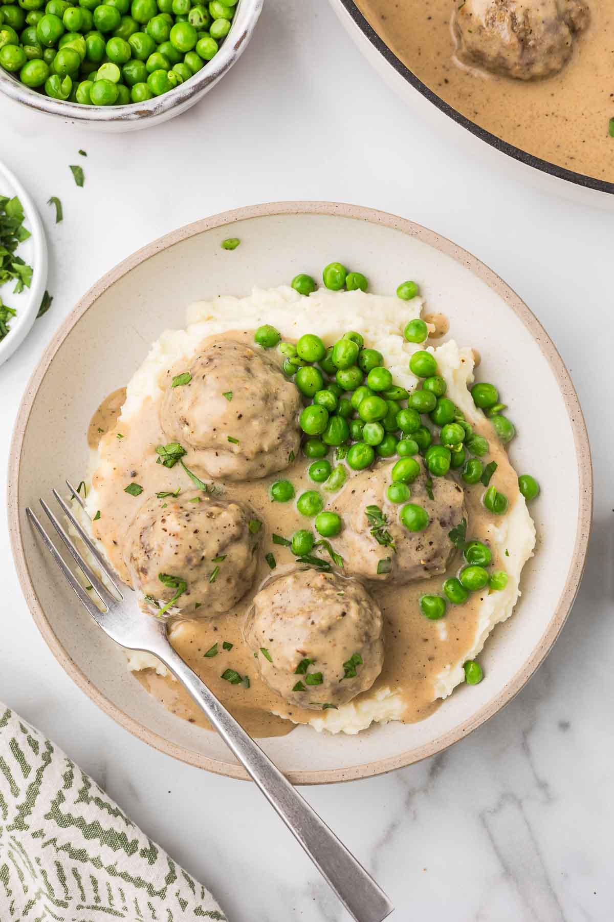Swedish meatballs served over mashed potatoes and a sprinkle of green peas.