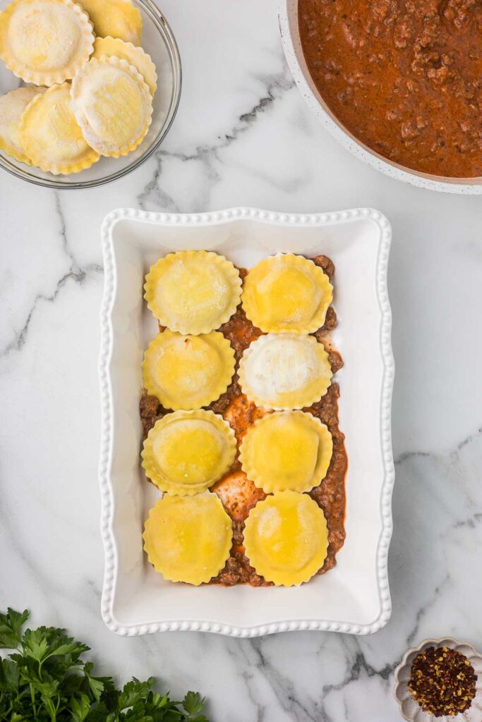 Frozen cheese ravioli in a casserole dish before adding sauce, cheese and a second layer of ravioli.