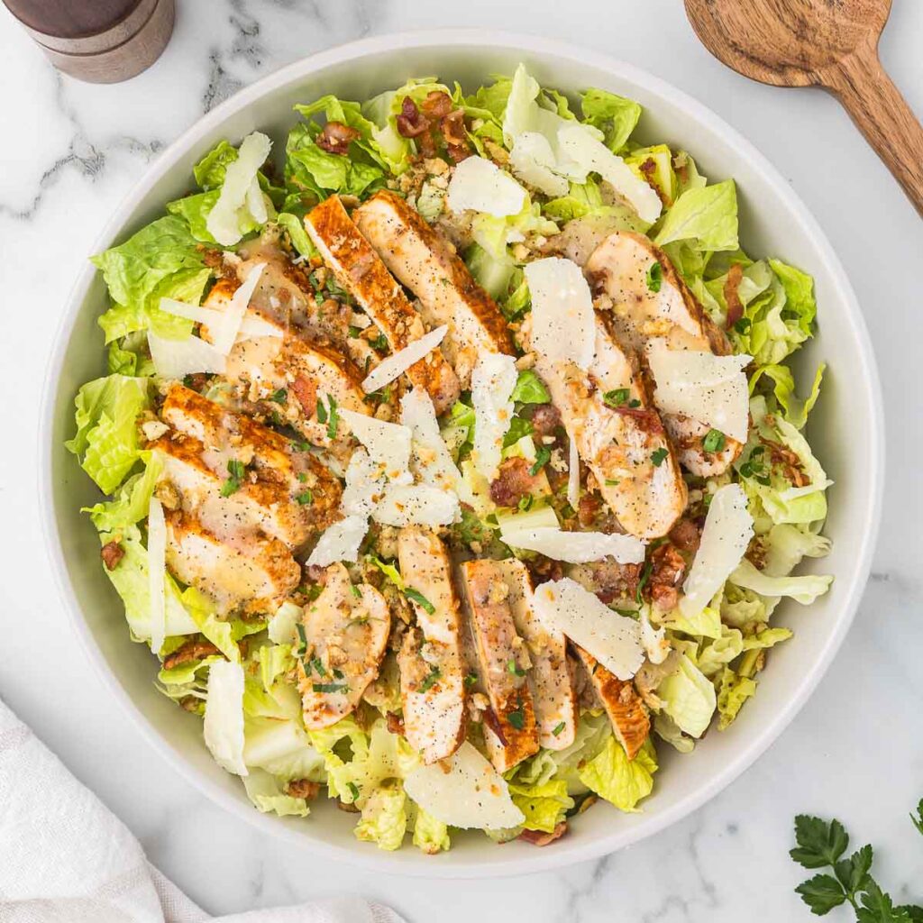 Chicken and bacon caesar salad in a white bowl with crunchy breadcrumbs.