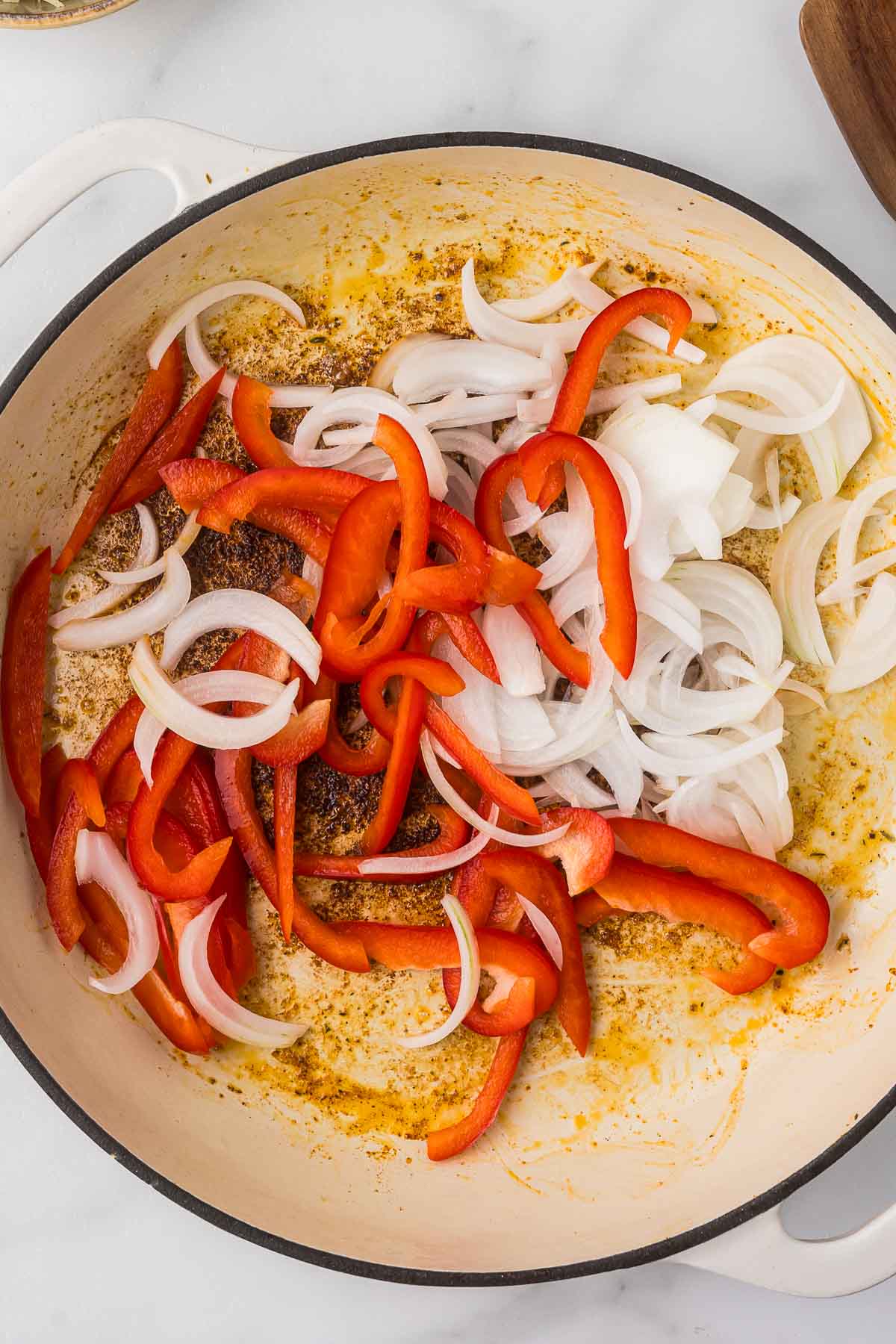 Sliced onions and red bell peppers in a pan with garlic.