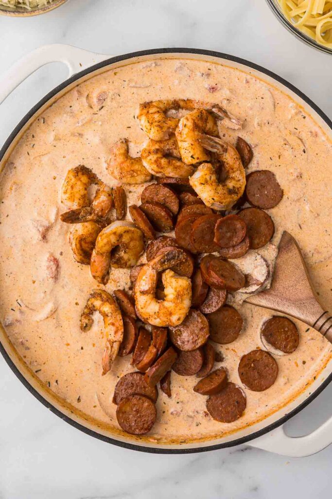 Cajun alfredo sauce with shrimp and sausage being added back to the pan before the pasta.