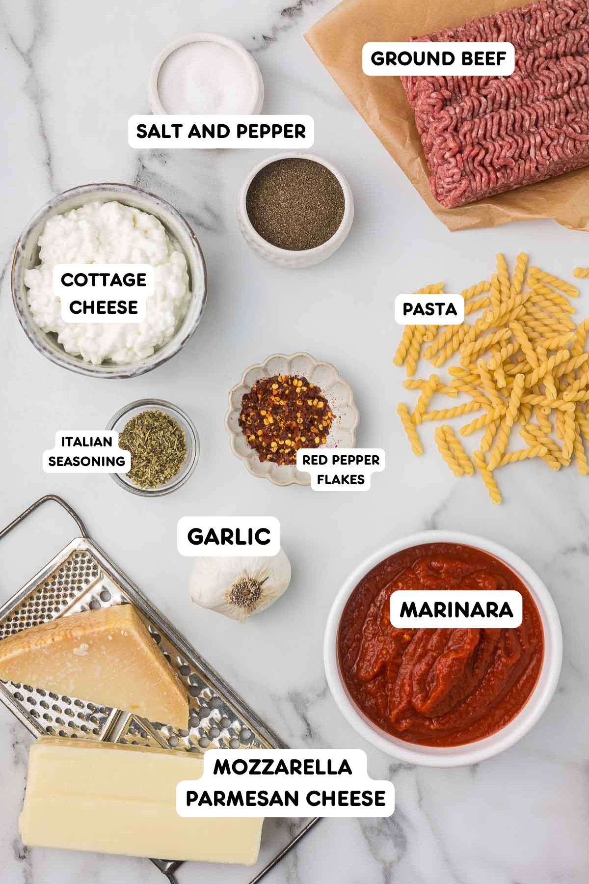 Ground beef, salt, pepper, chili flakes, Italian seasoning, cottage cheese, spiral pasta, garlic, marinara sauce, mozzarella cheese and parmesan cheese on a cheese grater. 