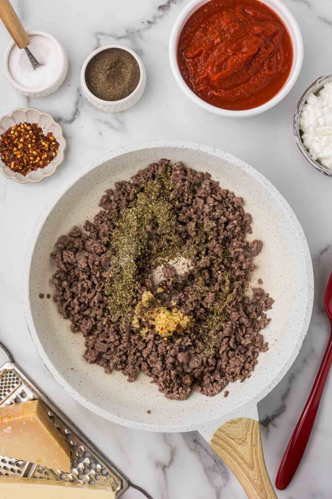 Browned ground beef with spices and garlic in a skillet.