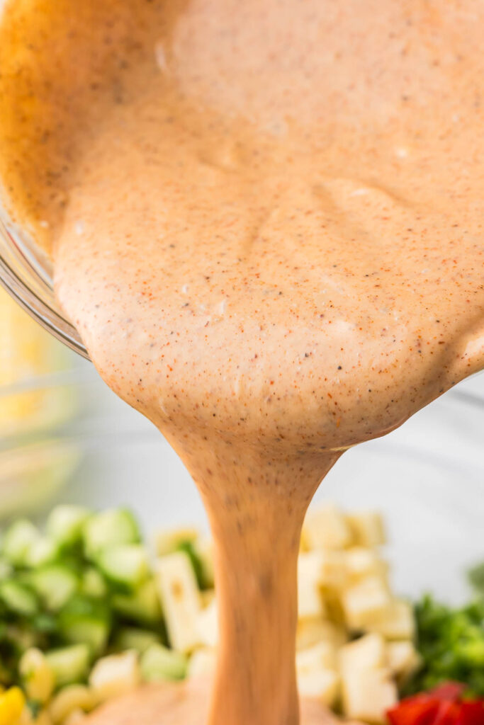 The dressing for mexican macaroni salad being poured over the salad.