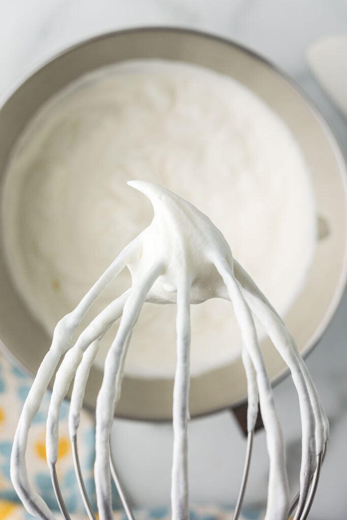 The whisk part of a kitchen aid with whipped cream on it showing soft peaks.