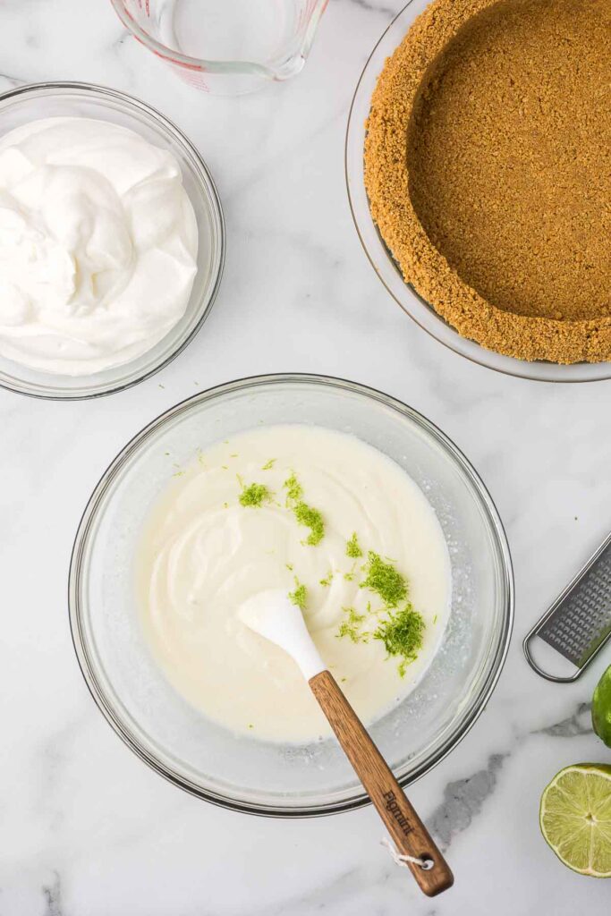 Sweetened condensed milk with lime juice and lime zest in a clear mixing bowl.