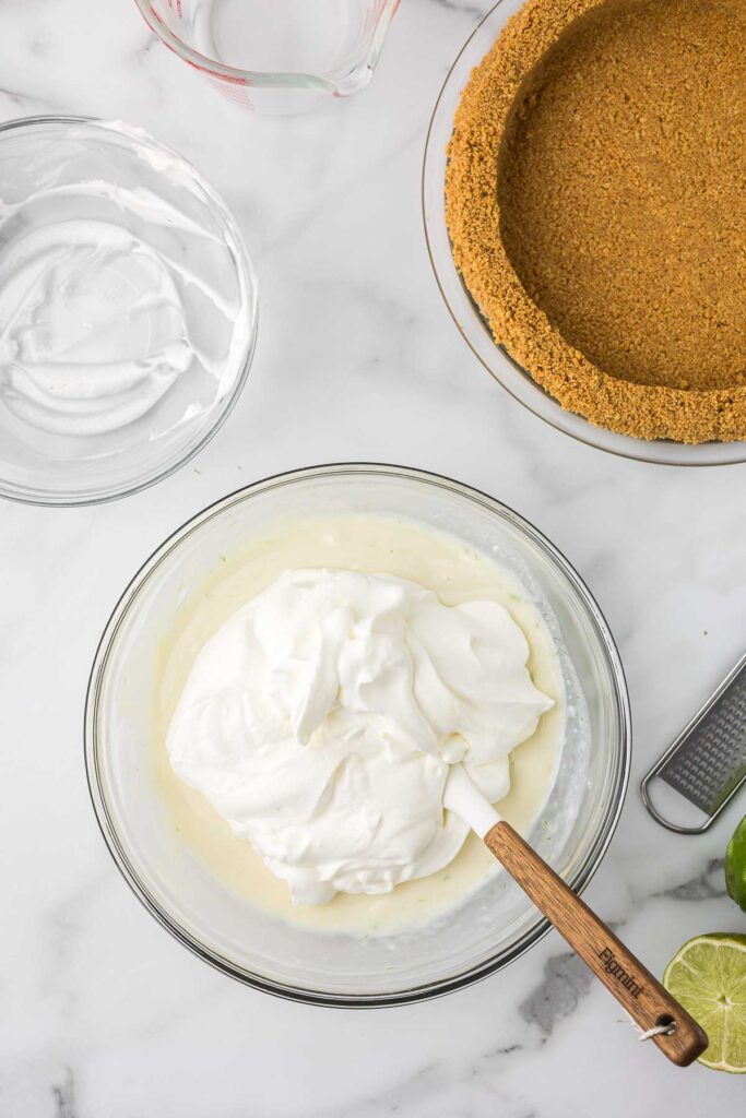 Clear mixing bowl with whipped topping being added to condensed milk and lime juice.