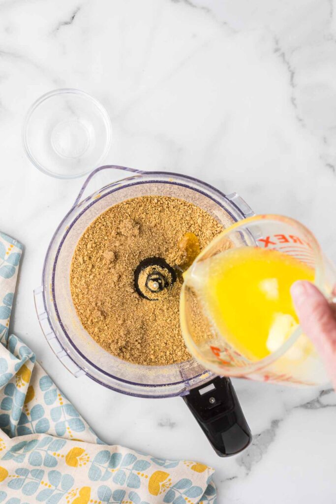 Graham crackers and brown sugar in a food processor with butter being added.