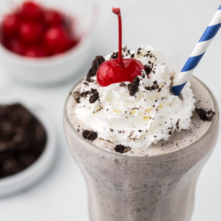 Oreo Cookie Milkshake with whipped cream, a cherry and cookie crumbles.