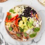 Pulled pork meal in a bowl including rice, cheese, beans, red bell peppers and slaw.