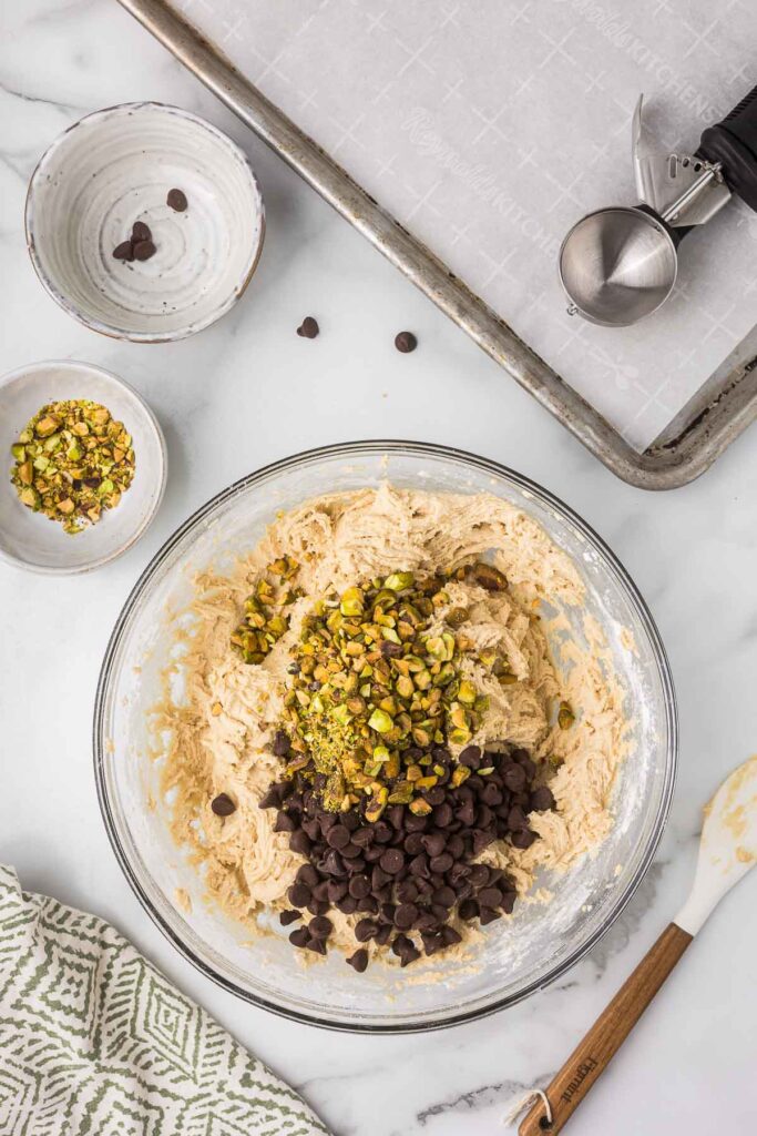 Milk chocolate chips and chopped pecans being mixed into cookie dough.