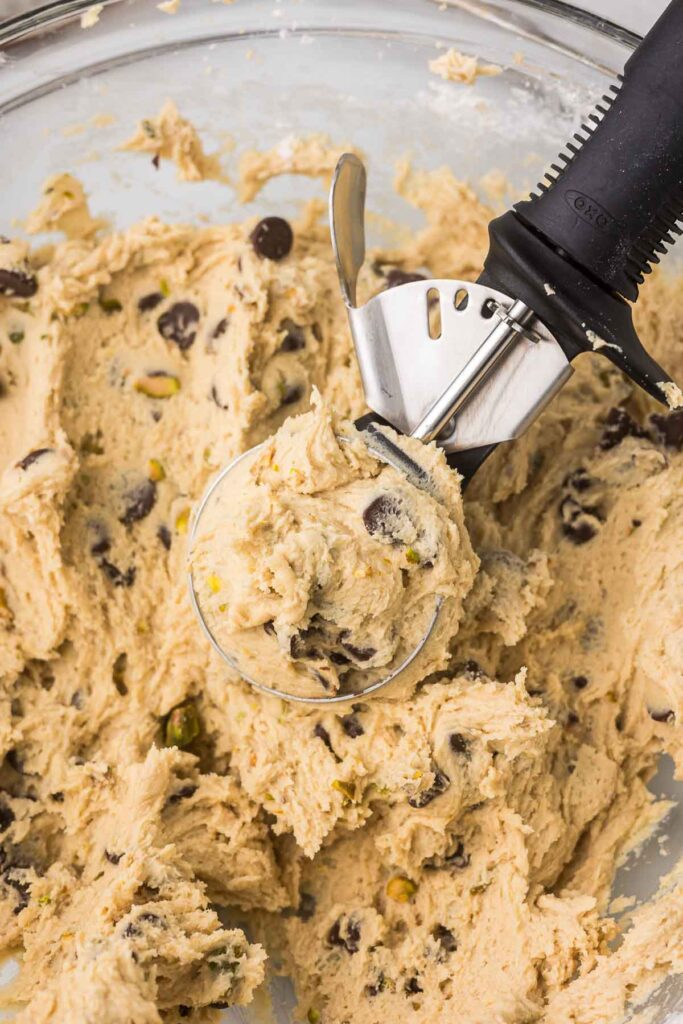 Cookie dough in a bowl with a jumbo cookie scoop in the bowl.