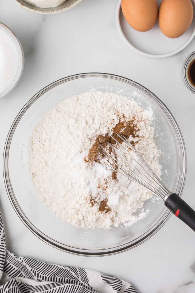 The dry mixture for muffins in a clear bowl with a wire wisk.