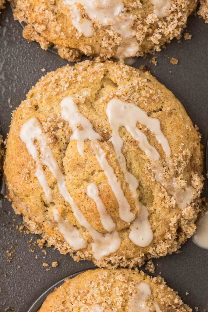 Cinnamon Roll Muffin in a muffin pan with a drizzle of glaze.