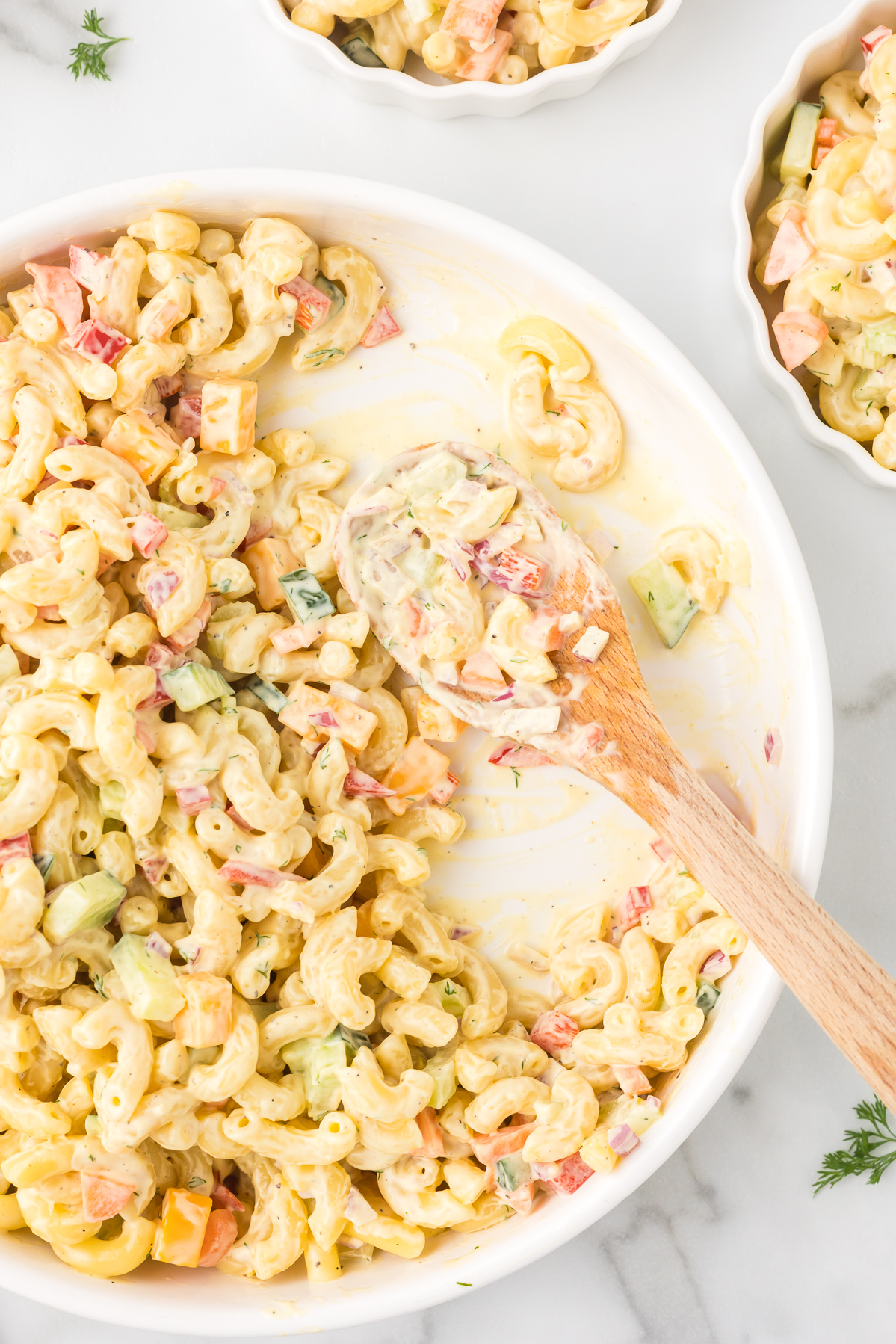 Macaroni salad with one portion removed and a wooden spoon in the dish.