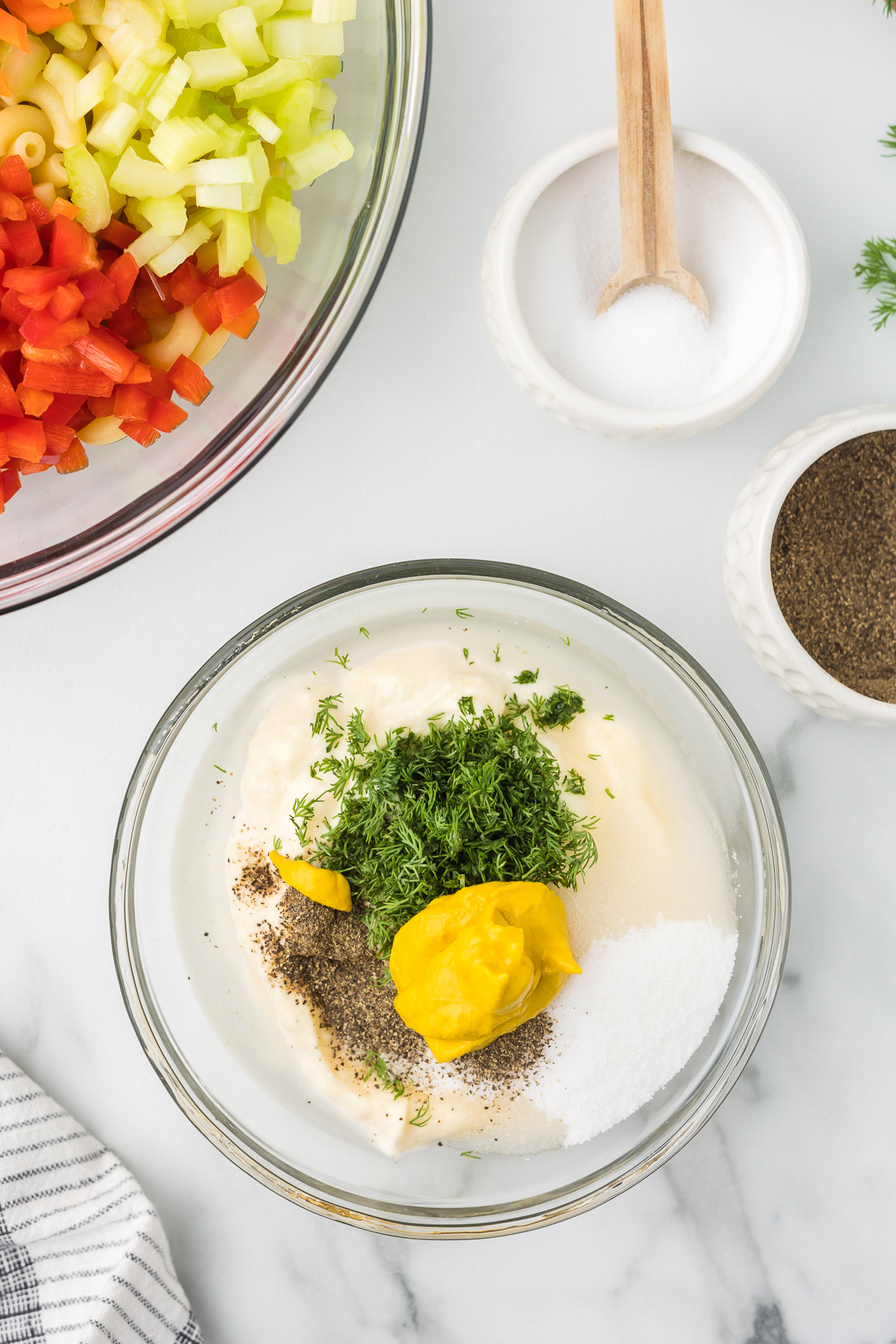 Mayonnaise salt, pepper, yellow mustard and fresh dill in a bowl before mixing to make macaroni salad.