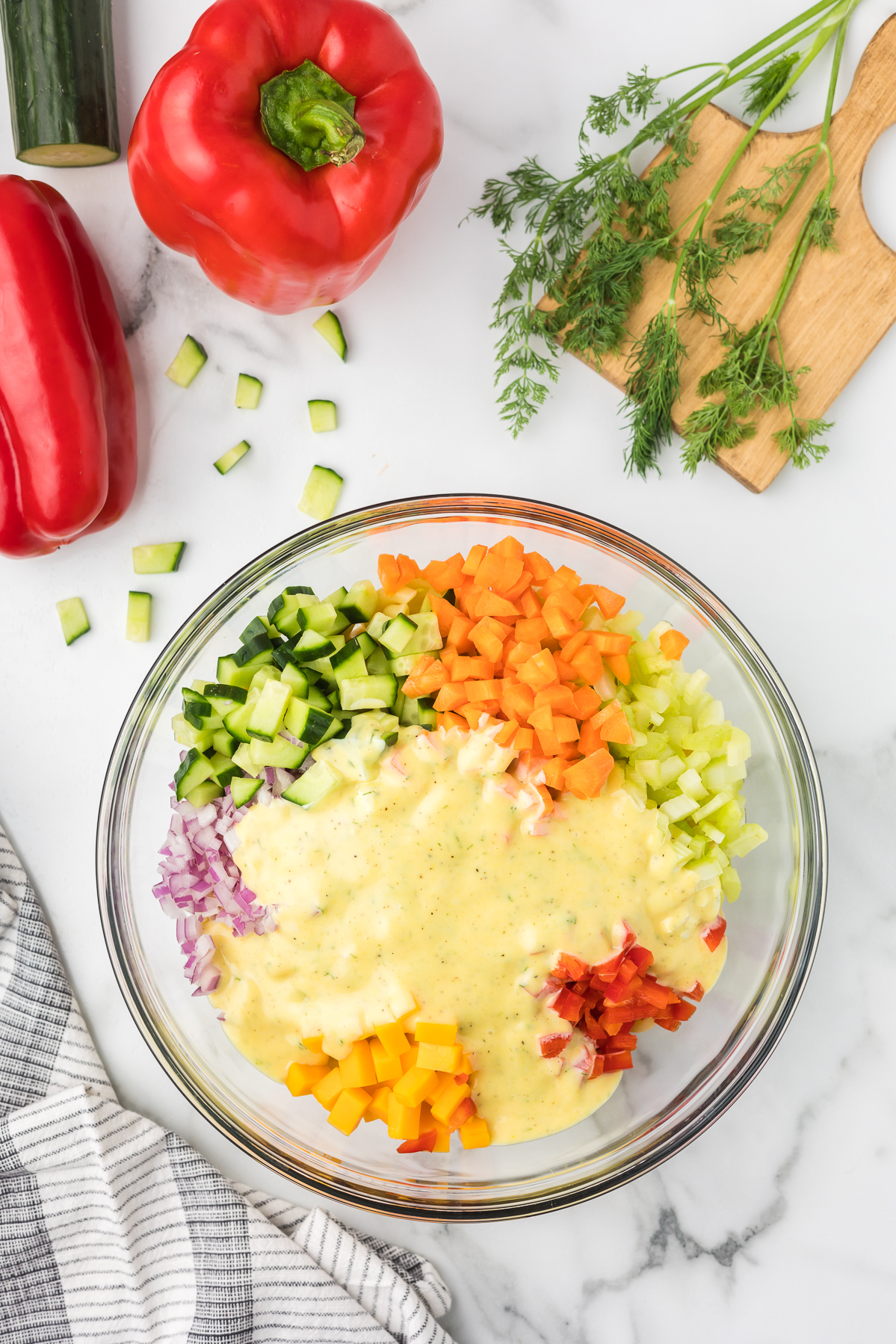 Carrots, celery, cucumber, red onion, cheese, red bell pepper and a creamy dressing in a clear bowl.