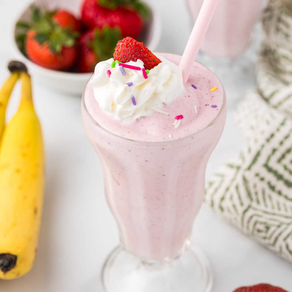 Strawberry Banana Milkshake with whipped cream and sprinkles in a malt glass.