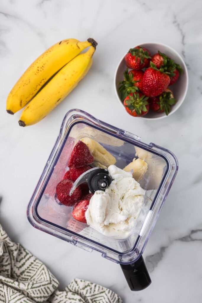 Ice cream, strawberries and banana in a blender before blending together.